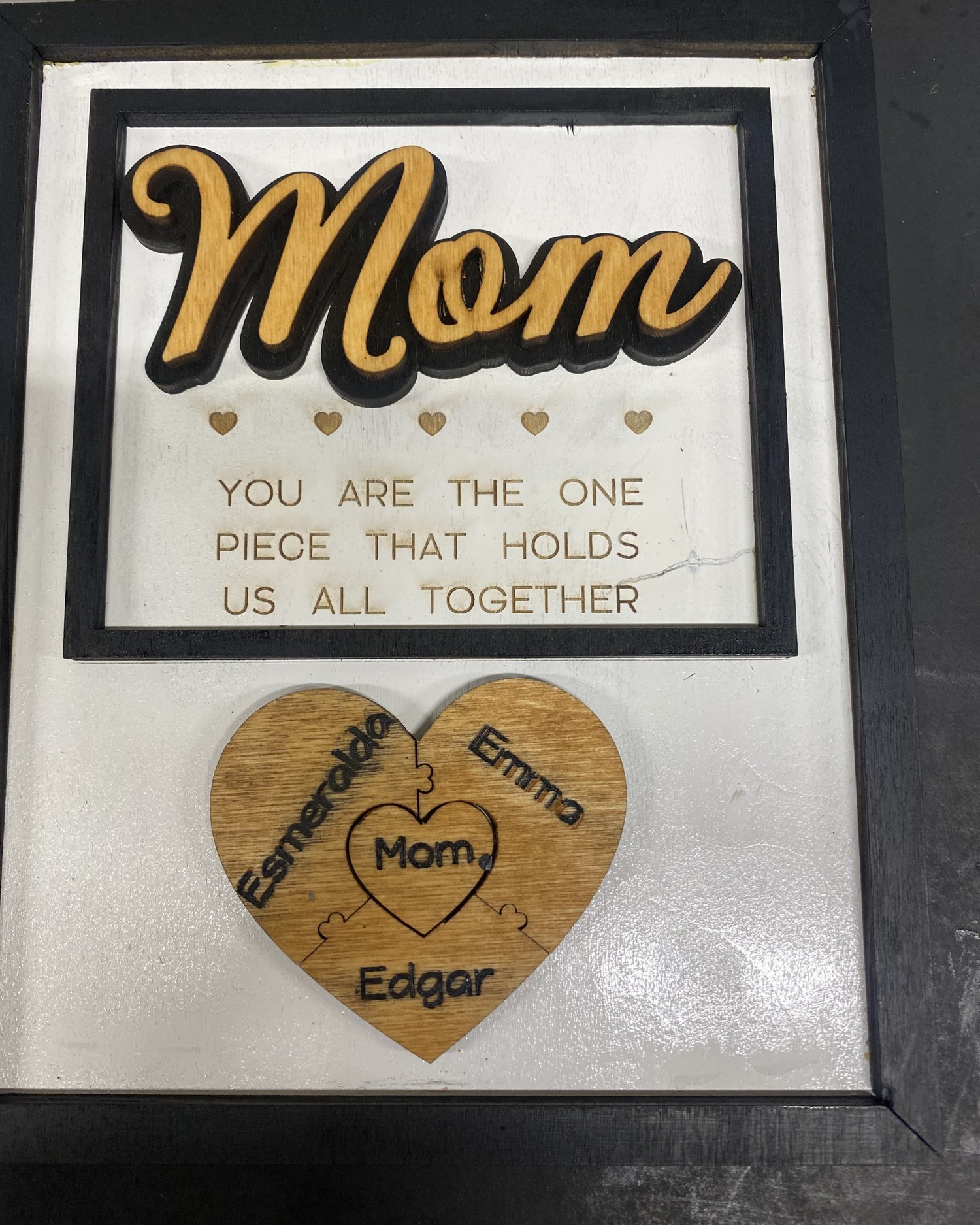 Layered wood plaque reading Mom, you are the one piece that holds us all together, with a puzzle heart engraved with three names
