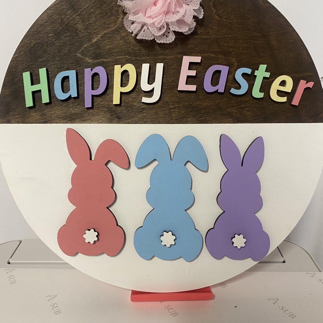 Round wooden Happy Easter sign with three pastel bunnies